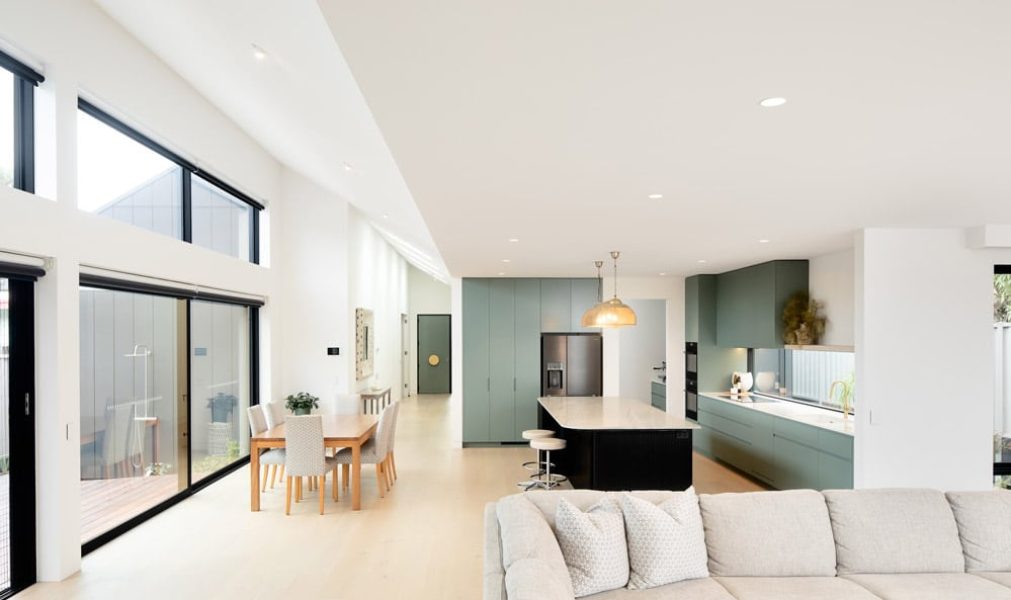A living space by home builders in Melbourne features cabinetry, a waterfall-edge kitchen island and pale oak floors.
