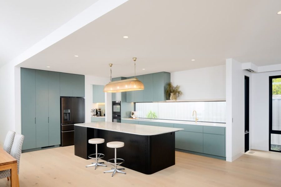 A modern kitchen by custom home builders in Melbourne features sage floor-to-ceiling cabinetry and a matte black island.