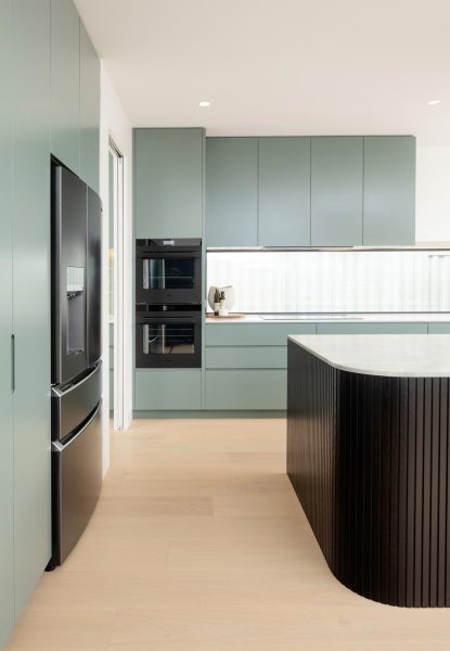 A galley kitchen in a bespoke custom home — showcasing sage-green handle-less cabinetry and matte-black appliances.