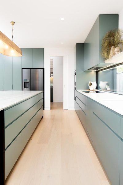 A galley kitchen in a bespoke custom home — showcasing sage-green handle-less cabinetry and matte-black appliances.