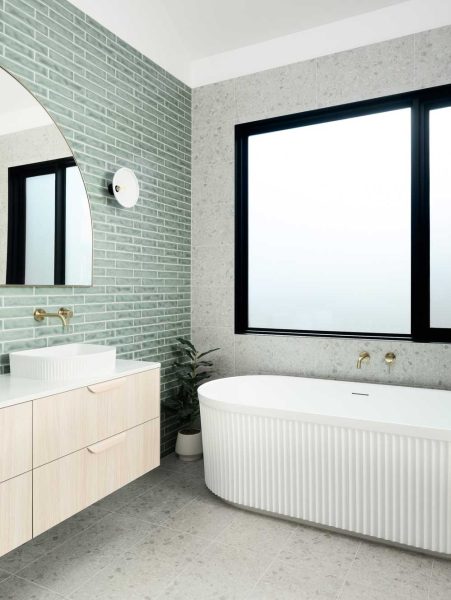 A contemporary bathroom showcasing home renovations in Melbourne with sage-green tiles and a fluted white freestanding bath.