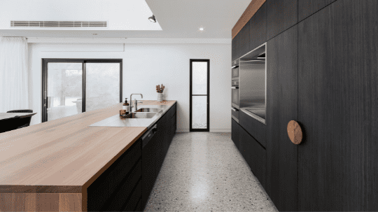 A stylish kitchen within a custom-built home by Spacemaker is marked by minimalist design and dark wood elements.