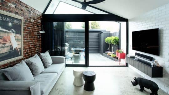 A renovation project features a charming living room with rustic brick walls and a glass door that leads to an outside area.