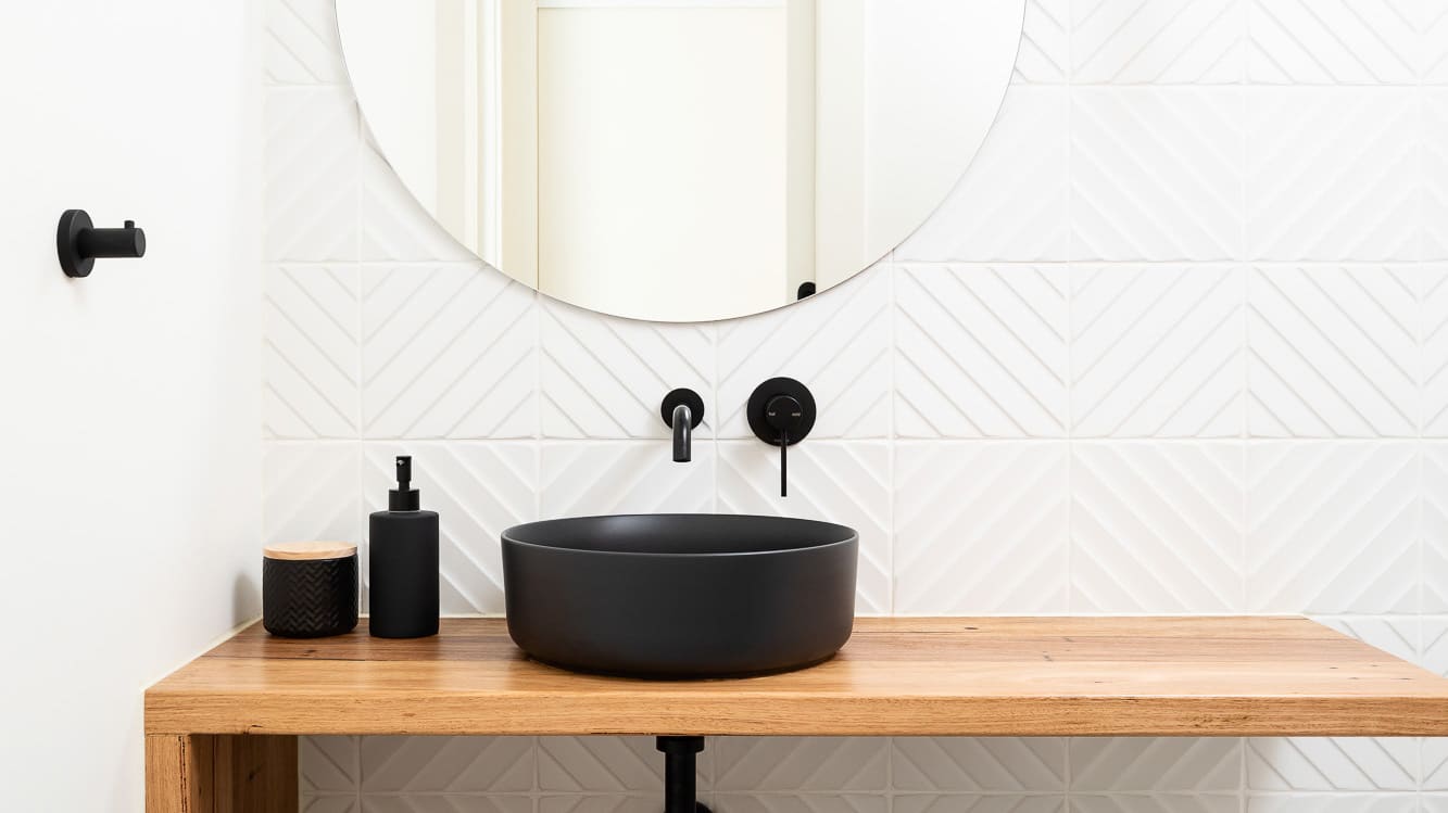 A bathroom vanity from the Kew High Street South Project features pristine white tiles and a black sink.